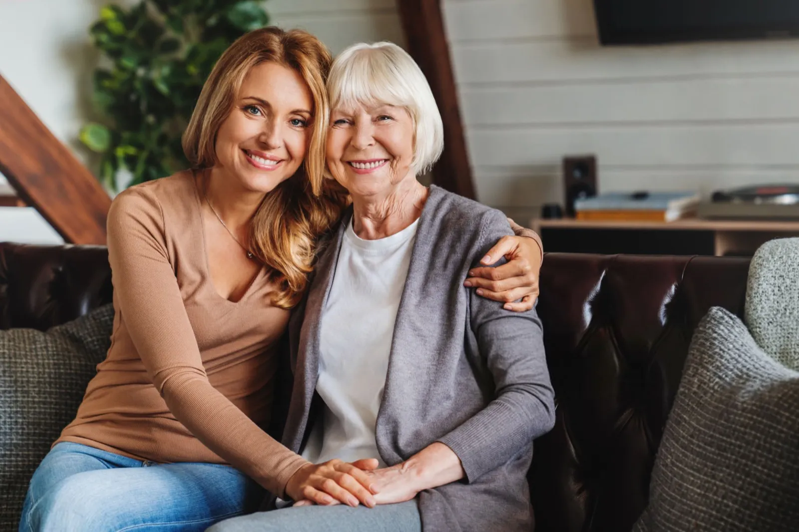 A caregiver sitting with her arm around a smiling older woman
